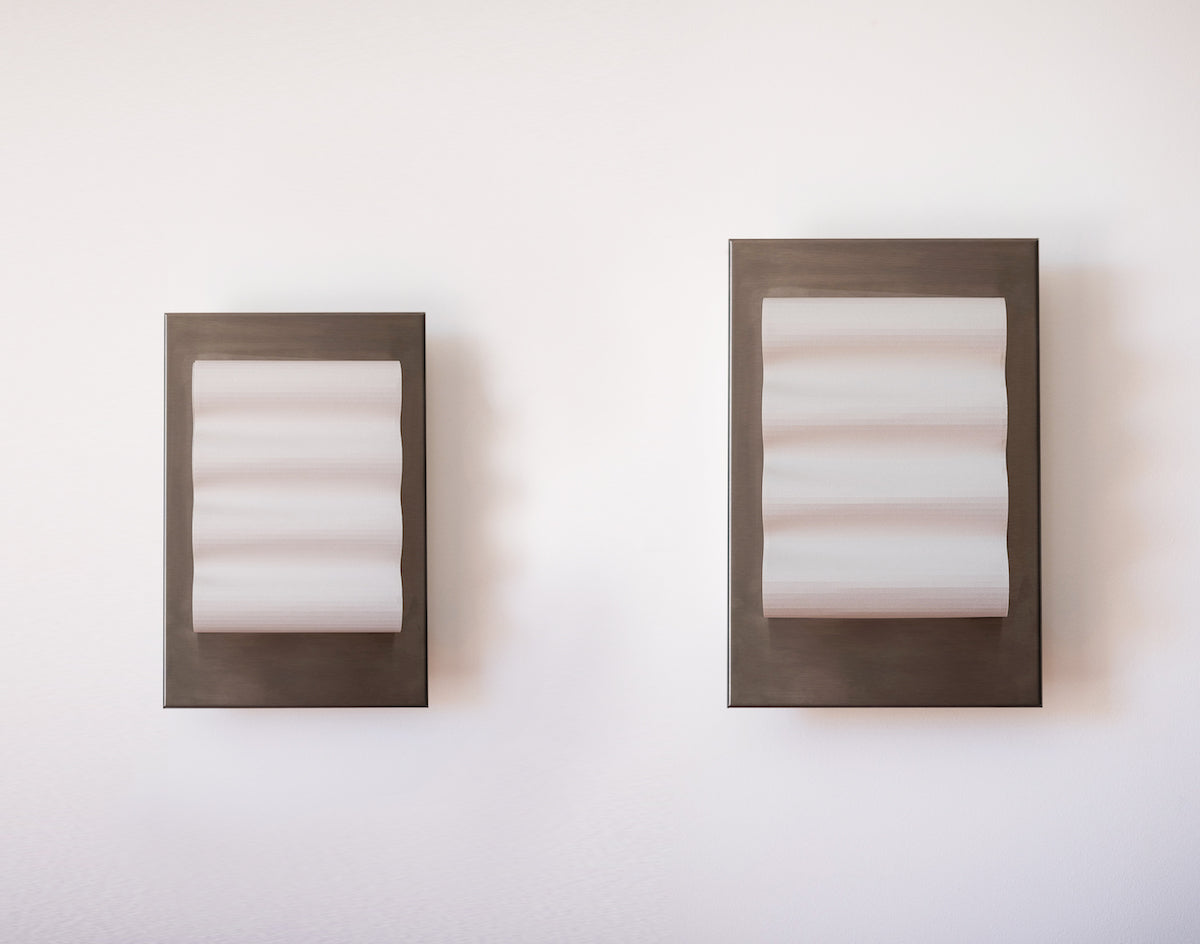 Les appliques Frame Alu Brut de Violaine d'Harcourt sont fabriquées à la main au Portugal, en aluminium et papier.  Dotées d'un design minimaliste et rendant un subtil hommage à l'architecture moderne, les appliques murales Frame sont réalisées avec des matériaux contrastés qui rehaussent le toucher doux d'une vague de papier.