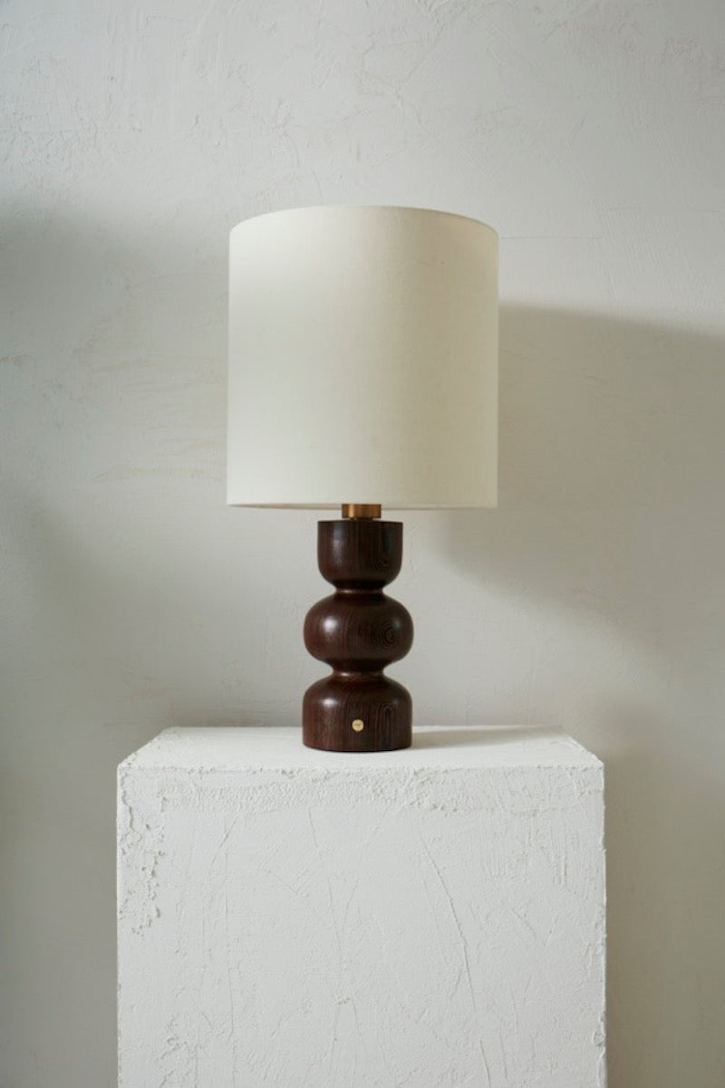 Les lignes pures, tout en rondeurs de la lampe Gilou, inspirées par les styles architecturaux des années 70, mettent en valeur le veinage zébré et profond du Wengé.&nbsp; Sa finition à la cire d'abeille apporte un rendu satiné et soyeux qui permet de préserver l'aspect naturel et authentique du bois, tout en le sublimant. L'abat jour écru permet de mettre en valeur le pied de lampe et apporte une lumière douce et diffuse.