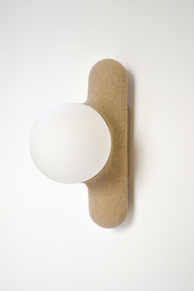 Intrigué par le figuier de barbarie qui se révèle être un outil naturel luttant contre l'érosion des sols, et participant à la préservation du territoire, Mickaël s'en inspire pour dessiner cette lampe. Volupté et douceur, sont les maîtres mots pour célébrer cette plante.  Modelée à partir de la terre que le figuier protège, l'applique Figue de Barbarie naît en terre cuite par la main du designer. Les opalines comme des baies charnues rayonnent, et mettent en lumière cette prouesse naturelle.