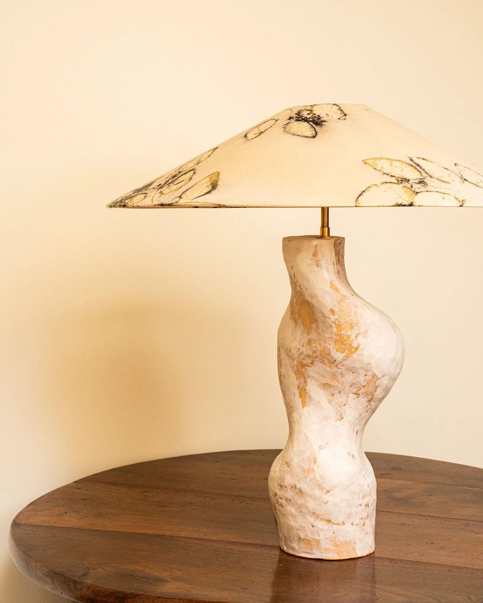Lampe à poser conçue et fabriquée par Marguerite Porche en collaboration avec Sandrina Rocha, artiste textile. Pied longiligne en grès blanc émaillé, surmonté d’un large abat-jour conique en soie teint naturellement à l’aide de végétaux.