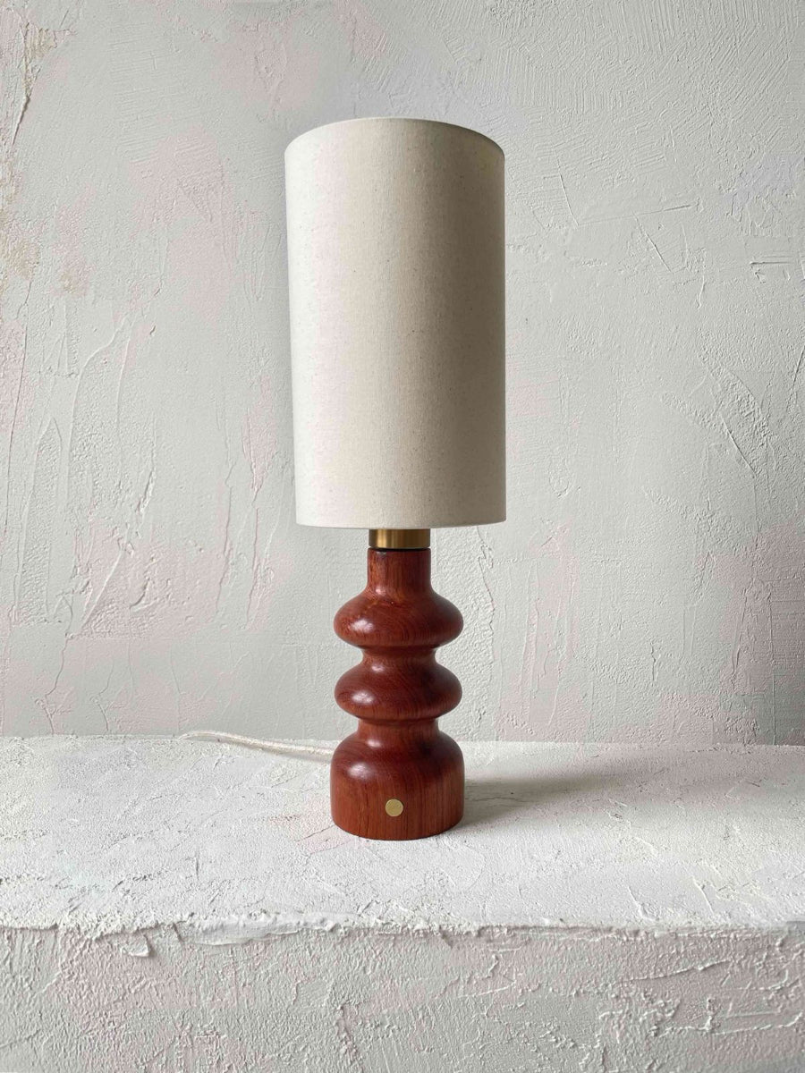 Elancée et raffinée, la lampe Alma séduit par la pureté de ses lignes et la chaleur profonde de son bois de Bubinga, aux reflets brun acajou. Son allure à la fois moderne et rétro, subtilement inspirée des années 70, lui confère une présence intemporelle qui s’adapte aussi bien aux petits espaces qu’aux grands intérieurs.
Existe aussi en essence Zebrano.

Sa finition à la cire d’abeille révèle la richesse du veinage et offre un toucher satiné et soyeux, préservant toute l’authenticité de la matière.