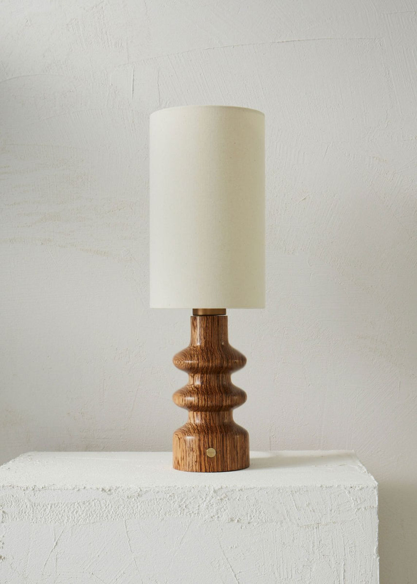 Elancée et raffinée, la lampe Alma séduit par la pureté de ses lignes et la chaleur profonde de son bois de Bubinga, aux reflets brun acajou. Son allure à la fois moderne et rétro, subtilement inspirée des années 70, lui confère une présence intemporelle qui s’adapte aussi bien aux petits espaces qu’aux grands intérieurs.
Existe aussi en essence Zebrano.

Sa finition à la cire d’abeille révèle la richesse du veinage et offre un toucher satiné et soyeux, préservant toute l’authenticité de la matière.