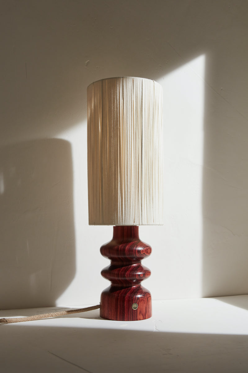 Les lignes pures et élancées de la lampe Alma , mettent en valeur le veinage brun rouge du Bubinga qui apporte une touche à la fois moderne et seventies à cette pièce qui s'adapte aussi bien aux petits qu'aux grands espaces.  Sa finition à la cire d'abeille apporte un rendu satiné et soyeux qui permet de préserver l'aspect naturel et authentique du bois, tout en le sublimant. L'abat jour écru permet de mettre en valeur le pied de lampe et d'apporter une lumière douce et diffuse.