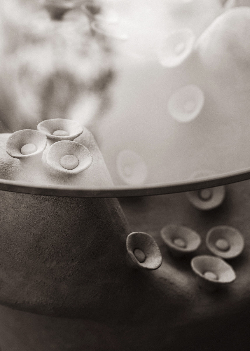 Table basse conçue et fabriquée par la céramiste Marguerite Porche. Deux larges pieds en grès blanc aux courbes sinueuses évoquant la roche sculptée par les éléments et parcourue de petites fleurs cherchant le soleil, portent un large plateau en verre d’un cm d’épaisseur. 