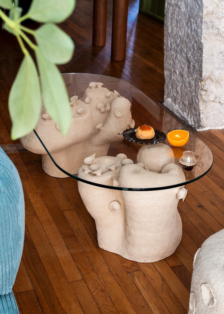 Table basse conçue et fabriquée par la céramiste Marguerite Porche. Deux larges pieds en grès blanc aux courbes sinueuses évoquant la roche sculptée par les éléments et parcourue de petites fleurs cherchant le soleil, portent un large plateau en verre d’un cm d’épaisseur. 