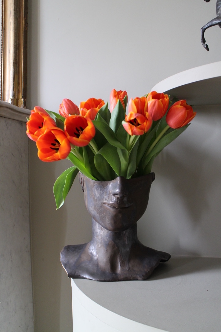 Vase Tête de Bronze by Thalia Dalecky, in glazed orange stoneware: a hand-sculpted face in high relief reveals golden reflections in the light, strength and delicacy fused between ceramic and bronze.