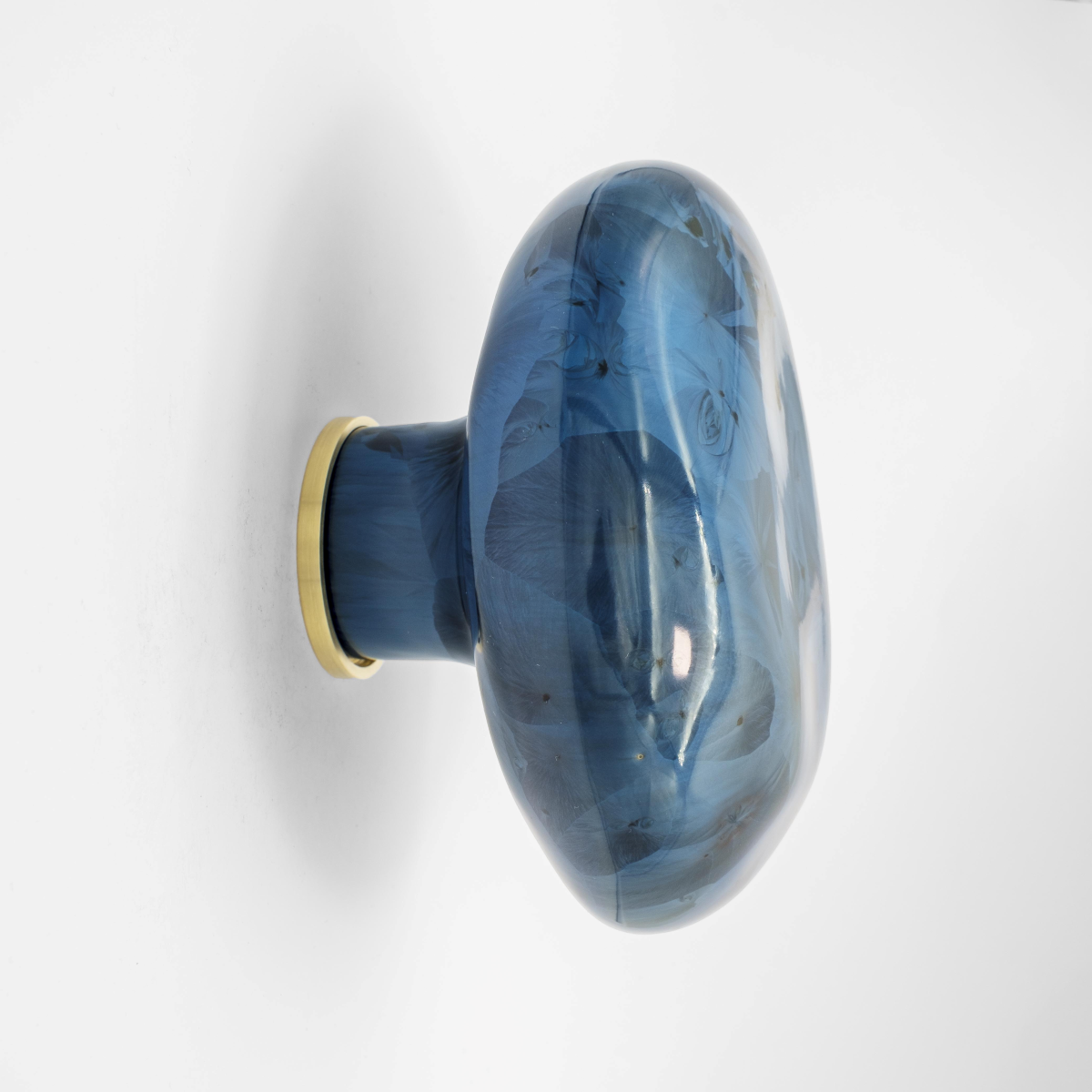 La patère Agate tire son nom de la pierre précieuse éponyme. Les Grecs et les Égyptiens l'utilisaient déjà dans la confection d'objets sacrés. Chaque patère possède sa propre personnalité, accentuée par les émaux cristallisés ou colorés qui s'harmonisent avec sa forme douce et organique, reflétant la diversité des teintes présentes dans les pierres d'Agate.

Son design intemporel et organique évoque la beauté et la simplicité des galets, tandis que sa délicate base est ornée d'une bague en laiton brossé