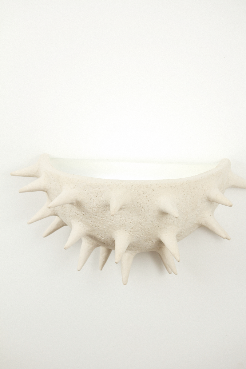 Cette applique Jupiter constituée de grès chamotte présente une texture avec des grains de sable. Chaque pièce est unique, numérotée, signée et modelée manuellement dans un grès chamotte, une argile cuite plusieurs fois entre 900 et 1400 degrés. Au cours de ce processus, l'objet devient aussi solide que la pierre. C'est par l'assemblage, le modelage, la sculpture et les différentes cuissons que l'objet se révèle.

Grâce à la céramique, Alan Louis capture l'essence particulière de l'élégance brute.