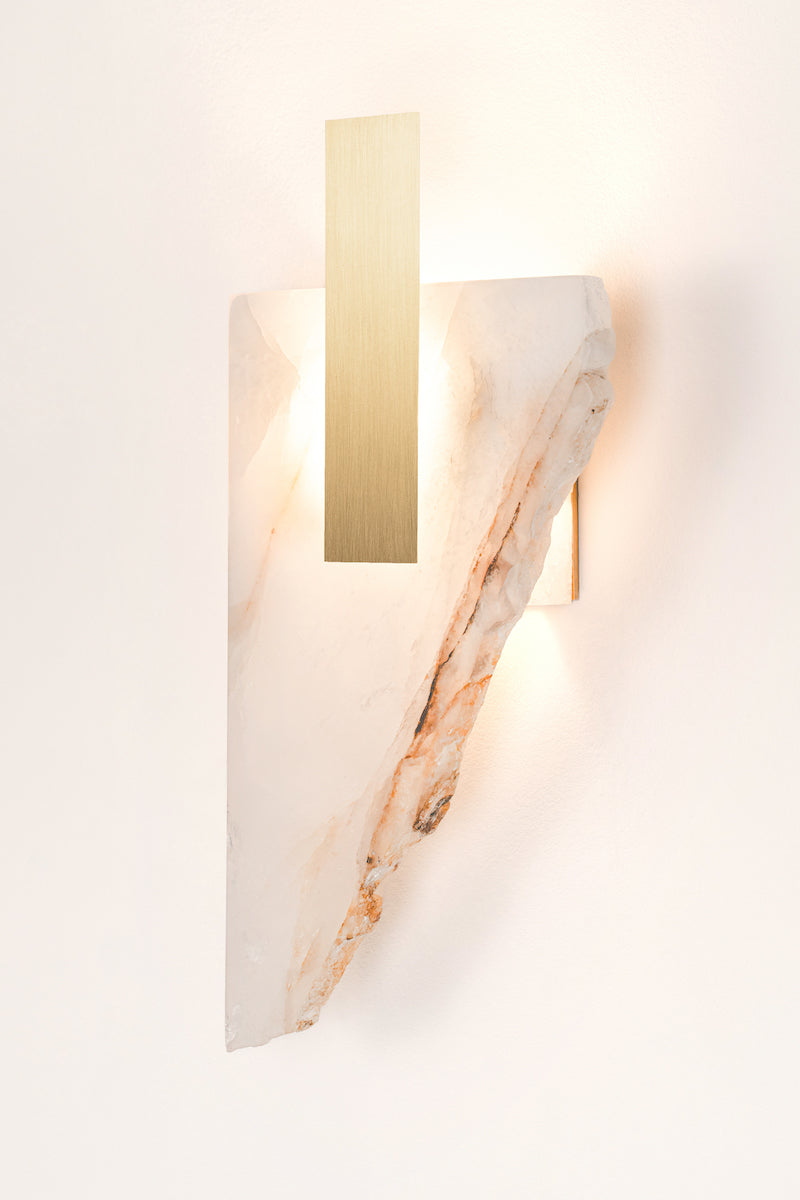 Applique Déchirée en golden quartzite et laiton, inspirée par la matière froissée, pliée puis déchirée du papier. Déchirée transpose cette tension fragile dans un langage minéral et lumineux.La pierre, traversée par la lumière, évoque une feuille arrachée dont les plis et les failles captent chaque variation lumineuse. Le laiton vient souligner la déchirure comme une ligne précieuse, révélant la beauté de l’accident et de l’irrégularité.