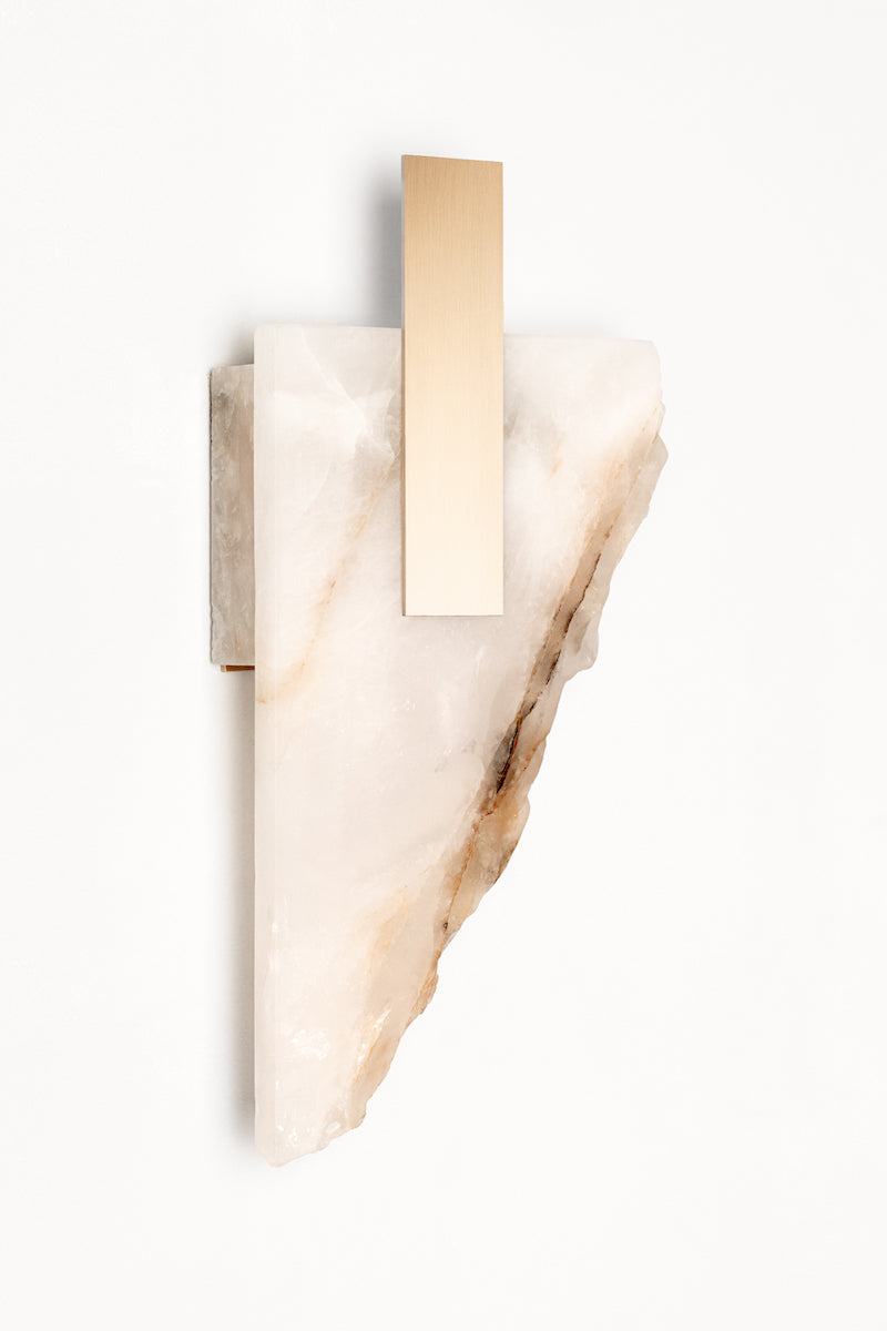 Applique Déchirée en golden quartzite et laiton, inspirée par la matière froissée, pliée puis déchirée du papier. Déchirée transpose cette tension fragile dans un langage minéral et lumineux.La pierre, traversée par la lumière, évoque une feuille arrachée dont les plis et les failles captent chaque variation lumineuse. Le laiton vient souligner la déchirure comme une ligne précieuse, révélant la beauté de l’accident et de l’irrégularité.