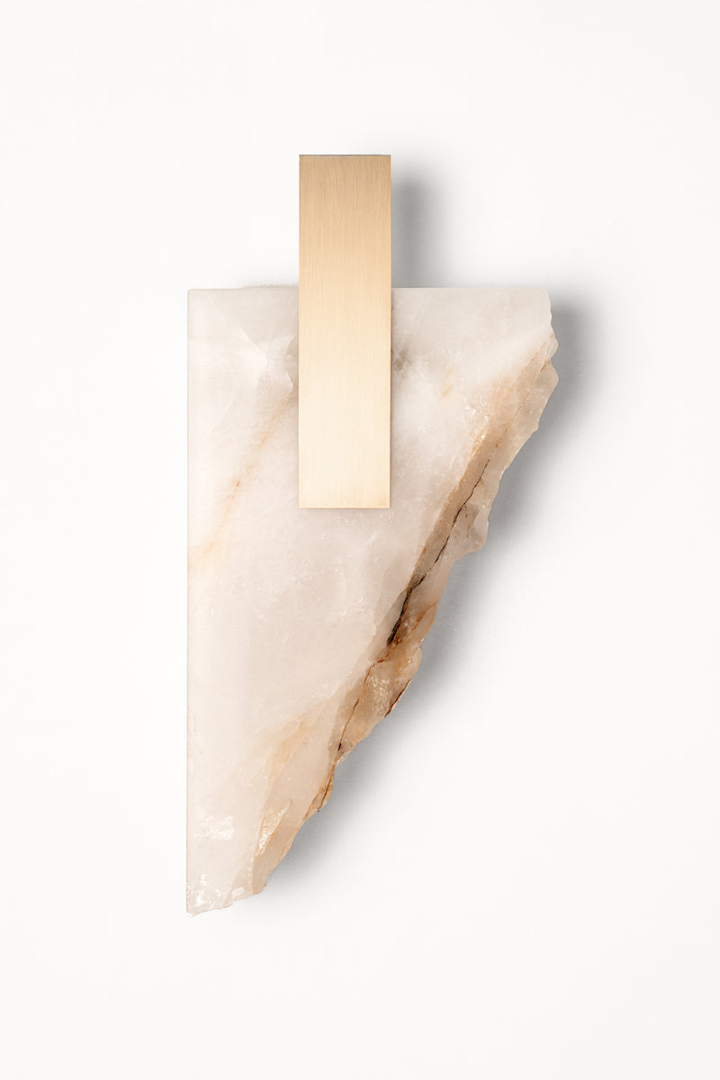 Applique Déchirée en golden quartzite et laiton, inspirée par la matière froissée, pliée puis déchirée du papier. Déchirée transpose cette tension fragile dans un langage minéral et lumineux.La pierre, traversée par la lumière, évoque une feuille arrachée dont les plis et les failles captent chaque variation lumineuse. Le laiton vient souligner la déchirure comme une ligne précieuse, révélant la beauté de l’accident et de l’irrégularité.