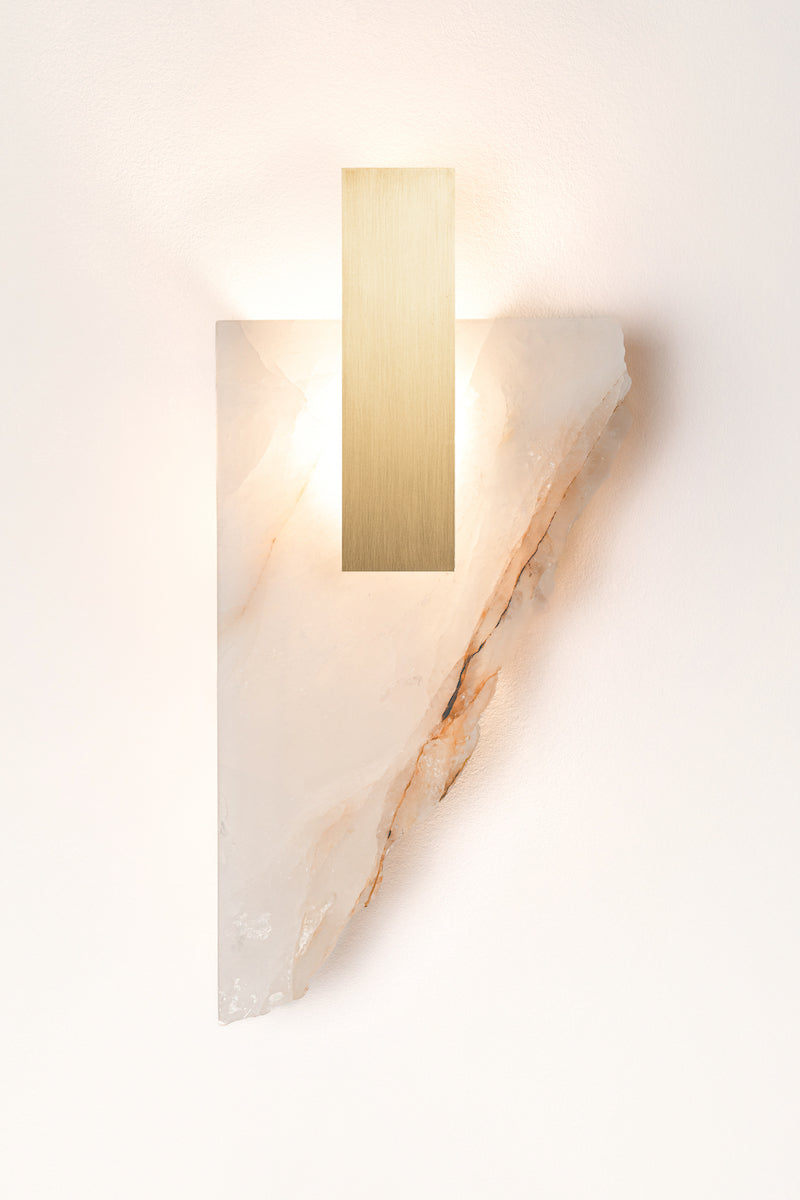 Applique Déchirée en golden quartzite et laiton, inspirée par la matière froissée, pliée puis déchirée du papier. Déchirée transpose cette tension fragile dans un langage minéral et lumineux.La pierre, traversée par la lumière, évoque une feuille arrachée dont les plis et les failles captent chaque variation lumineuse. Le laiton vient souligner la déchirure comme une ligne précieuse, révélant la beauté de l’accident et de l’irrégularité.