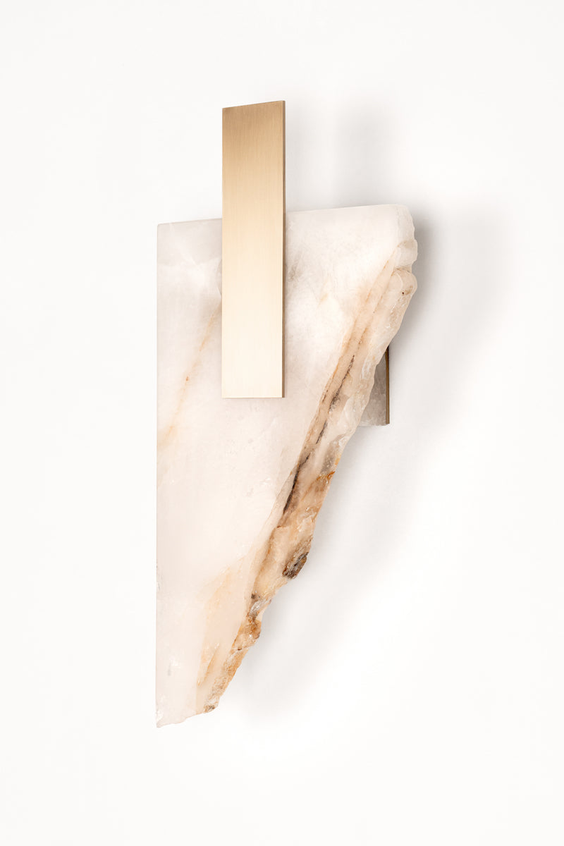 Applique Déchirée en golden quartzite et laiton, inspirée par la matière froissée, pliée puis déchirée du papier. Déchirée transpose cette tension fragile dans un langage minéral et lumineux.La pierre, traversée par la lumière, évoque une feuille arrachée dont les plis et les failles captent chaque variation lumineuse. Le laiton vient souligner la déchirure comme une ligne précieuse, révélant la beauté de l’accident et de l’irrégularité.