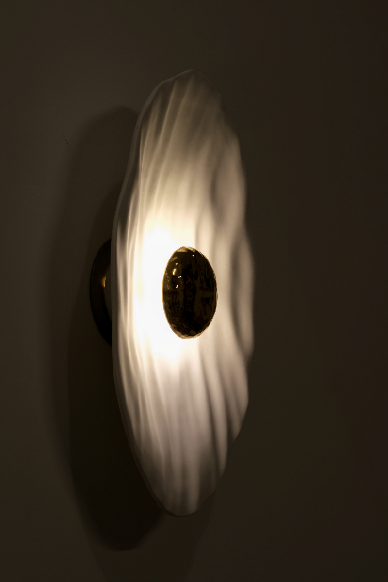 Façonnée à la main, l’applique Vesta associe un disque en faïence émaillée doré 24K, à une structure en plâtre sculpté aux lignes organiques.

Conçue comme une offrande à la lumière, Vesta rend hommage à la déesse du foyer. Elle diffuse une lumière douce et enveloppante, idéale pour instaurer une atmosphère apaisante et sacrée.