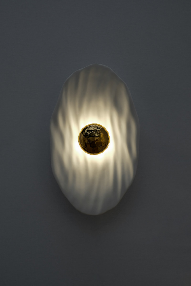 Façonnée à la main, l’applique Vesta associe un disque en faïence émaillée doré 24K, à une structure en plâtre sculpté aux lignes organiques.

Conçue comme une offrande à la lumière, Vesta rend hommage à la déesse du foyer. Elle diffuse une lumière douce et enveloppante, idéale pour instaurer une atmosphère apaisante et sacrée.