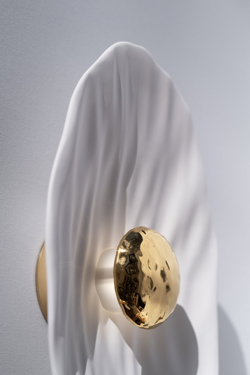 Façonnée à la main, l’applique Vesta associe un disque en faïence émaillée doré 24K, à une structure en plâtre sculpté aux lignes organiques.

Conçue comme une offrande à la lumière, Vesta rend hommage à la déesse du foyer. Elle diffuse une lumière douce et enveloppante, idéale pour instaurer une atmosphère apaisante et sacrée.