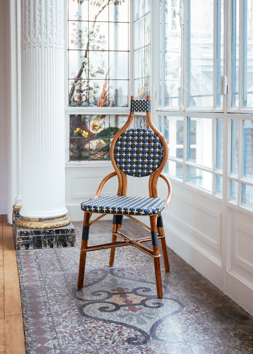 La chaise Odette fait la part belle au rotin. Le Second Empire a vu se développer le métier de rotinier et a été l’âge d’or de ce matériau. Le rotin est une tige de palmier importée des forêts tropicales asiatiques à l’époque coloniale. La chaise de bistro en rotin symbolise à elle seule les terrasses parisiennes et la gaieté de la capitale française. La forme florale et l’utilisation de matières végétales pour le design de la chaise Odette est une référence au catleya.