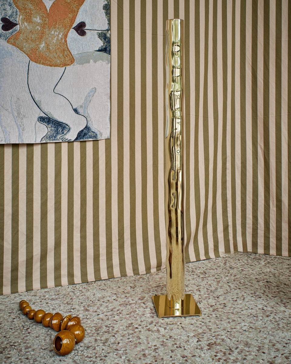 Hélios est un lampadaire sculptural en laiton poli miroir, non verni. Sa source lumineuse, dissimulée, diffuse une lumière douce vers le haut. Entièrement formée, soudée et polie à la main, chaque pièces de cette série sont uniques. Le reflet de sa hauteur dans son socle crée une illusion de mouvement, d’infini, un jeu de perceptions où le vertige s’invite. Hélios transforme l’espace, oscillant entre objet fonctionnel et œuvre sculpturale.