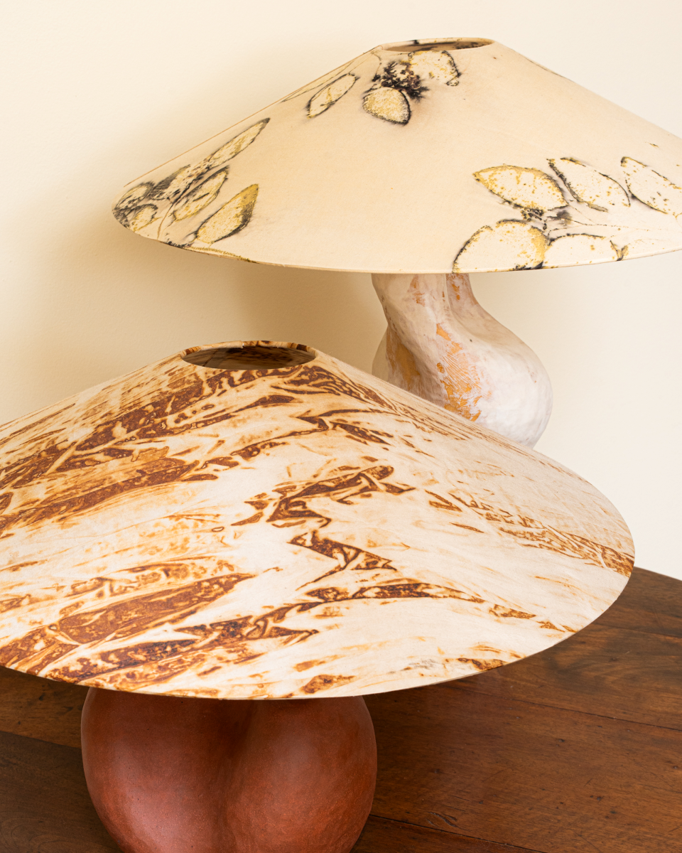 Lampe à poser conçue et fabriquée par Marguerite Porche en collaboration avec Sandrina Rocha, artiste textile. Pied en grès rouge brut de forme ronde, enveloppante, surmonté d’un large abat-jour conique en soie teint naturellement à l’aide de végétaux.
