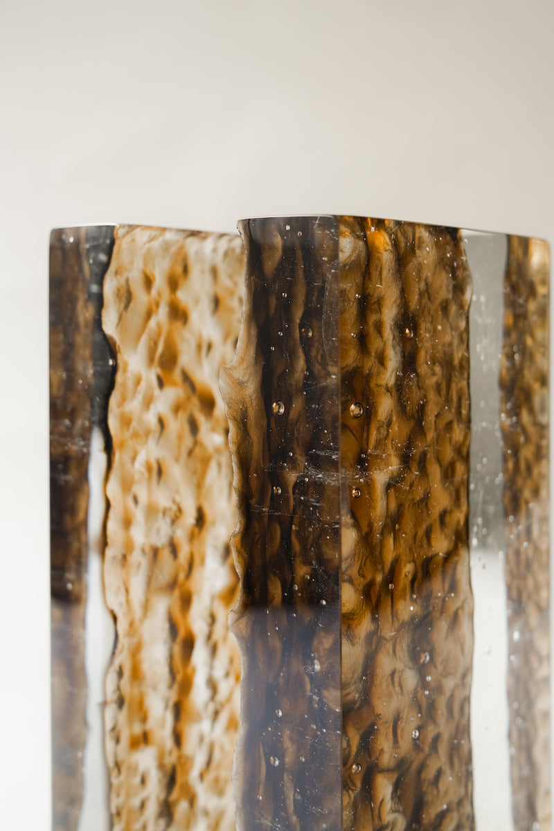 Bougeoir Géoda, réalisé en collaboration avec le verrier Matthieu Gicquel, née d’un dialogue entre matière, lumière et savoir-faire verrier. Inspirée des géodes naturelles, elle explore cette idée de beauté cachée, révélée au cœur de la matière.
À travers un verre travaillé en épaisseur, la collection retranscrit une dualité entre force minérale et délicatesse lumineuse. La matière joue avec la lumière, la capte, la filtre et la diffuse, créant des profondeurs, des reflets et des transparences qui évoluent 