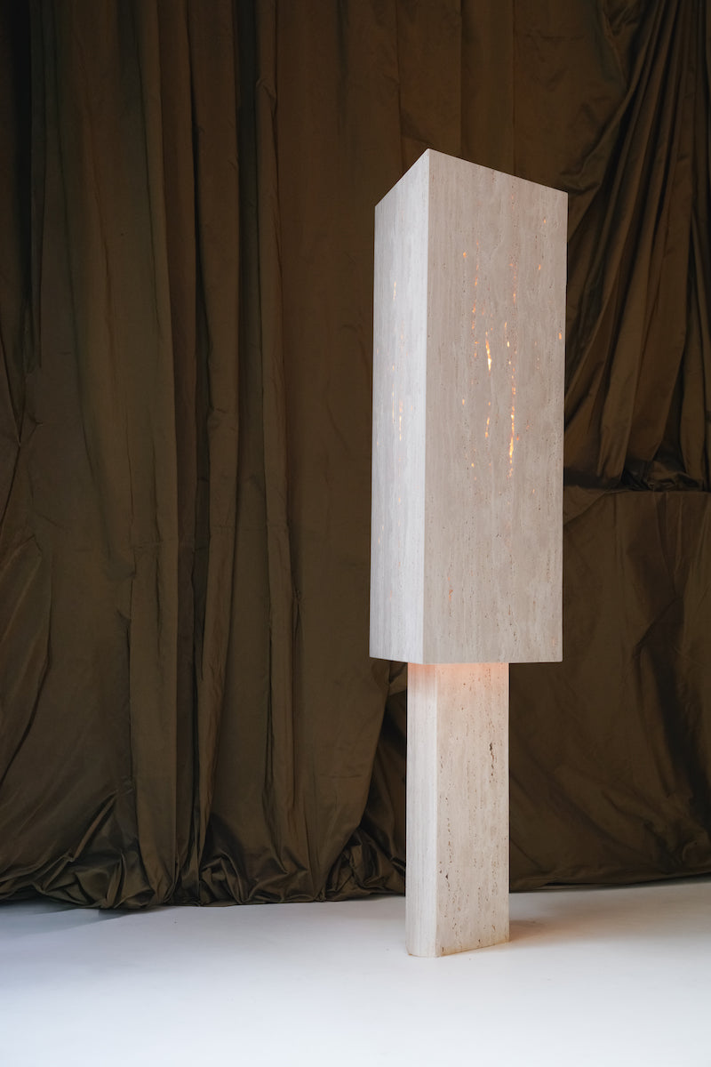 Lampe à poser Lucentia en travertin est née d’une recherche autour de la matière et de la lumière : réussir à faire traverser la lumière à une pierre habituellement perçue comme opaque, pour en révéler une beauté insoupçonnée.
Traversée par la lumière, la matière dévoile alors son paysage intérieur : ses fines aspérités, ses cristallisations, ses microcavités habituellement invisibles. La pierre semble changer de nature, passant d’un matériau dense et minéral à une présence presque vivante et aérienne.