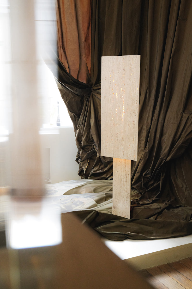 Lampe à poser Lucentia en travertin est née d’une recherche autour de la matière et de la lumière : réussir à faire traverser la lumière à une pierre habituellement perçue comme opaque, pour en révéler une beauté insoupçonnée.
Traversée par la lumière, la matière dévoile alors son paysage intérieur : ses fines aspérités, ses cristallisations, ses microcavités habituellement invisibles. La pierre semble changer de nature, passant d’un matériau dense et minéral à une présence presque vivante et aérienne.