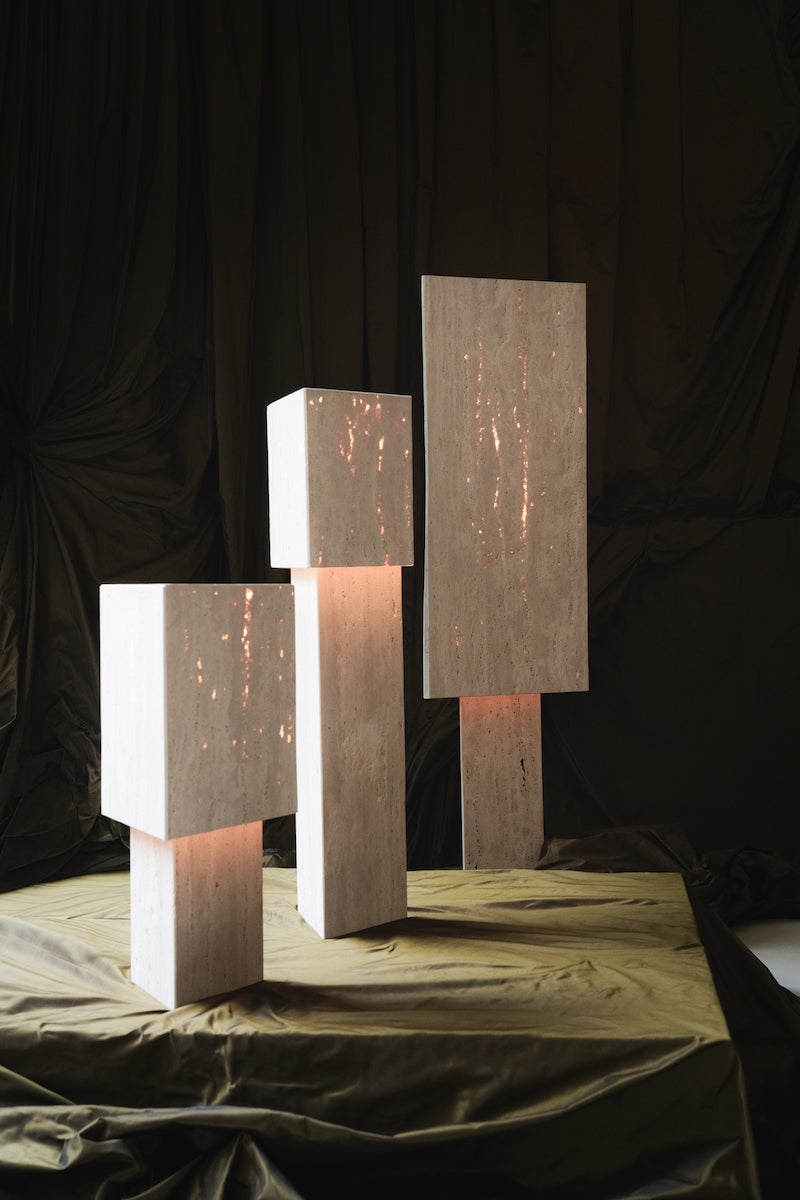 Lampe à poser Lucentia en travertin est née d’une recherche autour de la matière et de la lumière : réussir à faire traverser la lumière à une pierre habituellement perçue comme opaque, pour en révéler une beauté insoupçonnée.
Traversée par la lumière, la matière dévoile alors son paysage intérieur : ses fines aspérités, ses cristallisations, ses microcavités habituellement invisibles. La pierre semble changer de nature, passant d’un matériau dense et minéral à une présence presque vivante et aérienne.