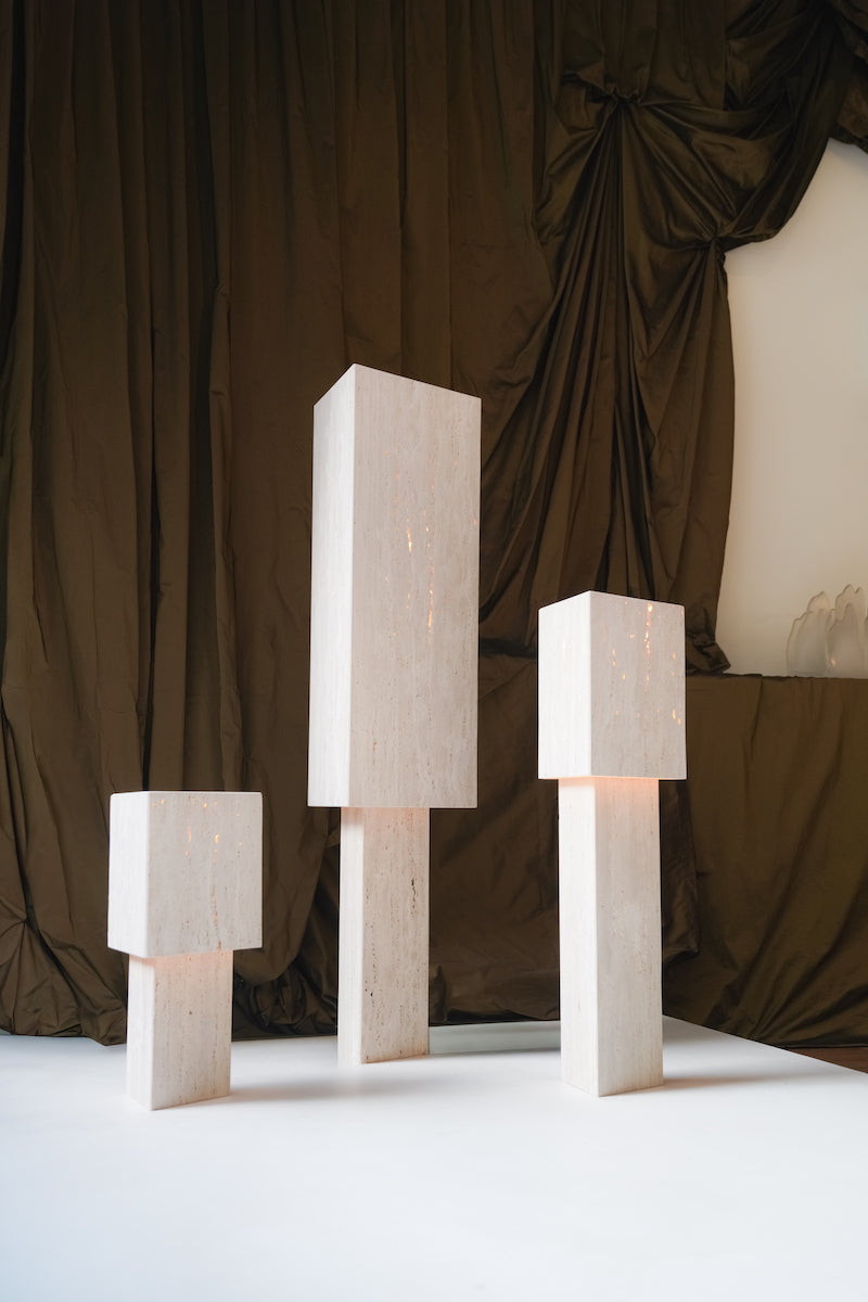 Lampe à poser Lucentia en travertin est née d’une recherche autour de la matière et de la lumière : réussir à faire traverser la lumière à une pierre habituellement perçue comme opaque, pour en révéler une beauté insoupçonnée.
Traversée par la lumière, la matière dévoile alors son paysage intérieur : ses fines aspérités, ses cristallisations, ses microcavités habituellement invisibles. La pierre semble changer de nature, passant d’un matériau dense et minéral à une présence presque vivante et aérienne.