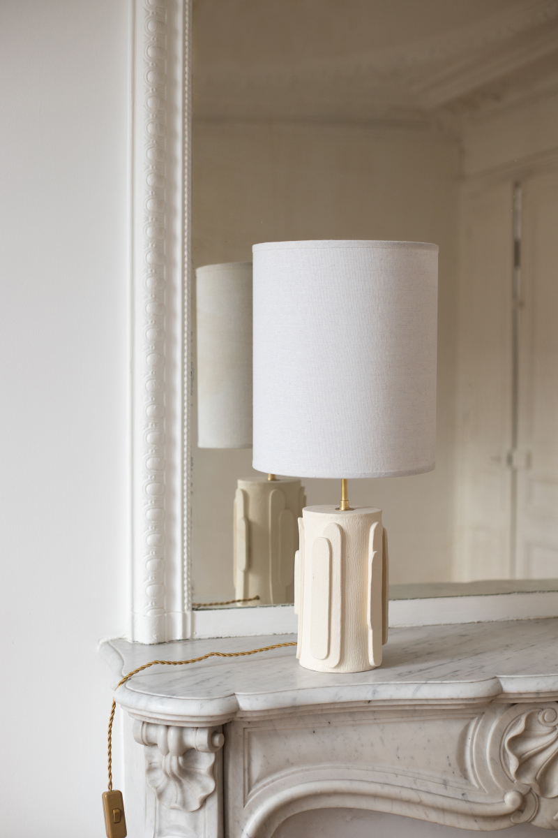 La lampe Glow en exclusivité chez Caroline Andréoni La Maison, tire son nom de l'éclat qu'il apporte, en anglais, évoquant ainsi la luminosité naturelle qui inspire infatigablement la créatrice Adeline Delesalle. Cette lampe est réalisée selon la technique de la plaque, résultat du savoir-faire de l'artiste, entièrement réalisée à la main dans ses ateliers en France. Les cylindres sont "griffés" afin de créer un contraste de matière entre le support et les éléments ajoutés.