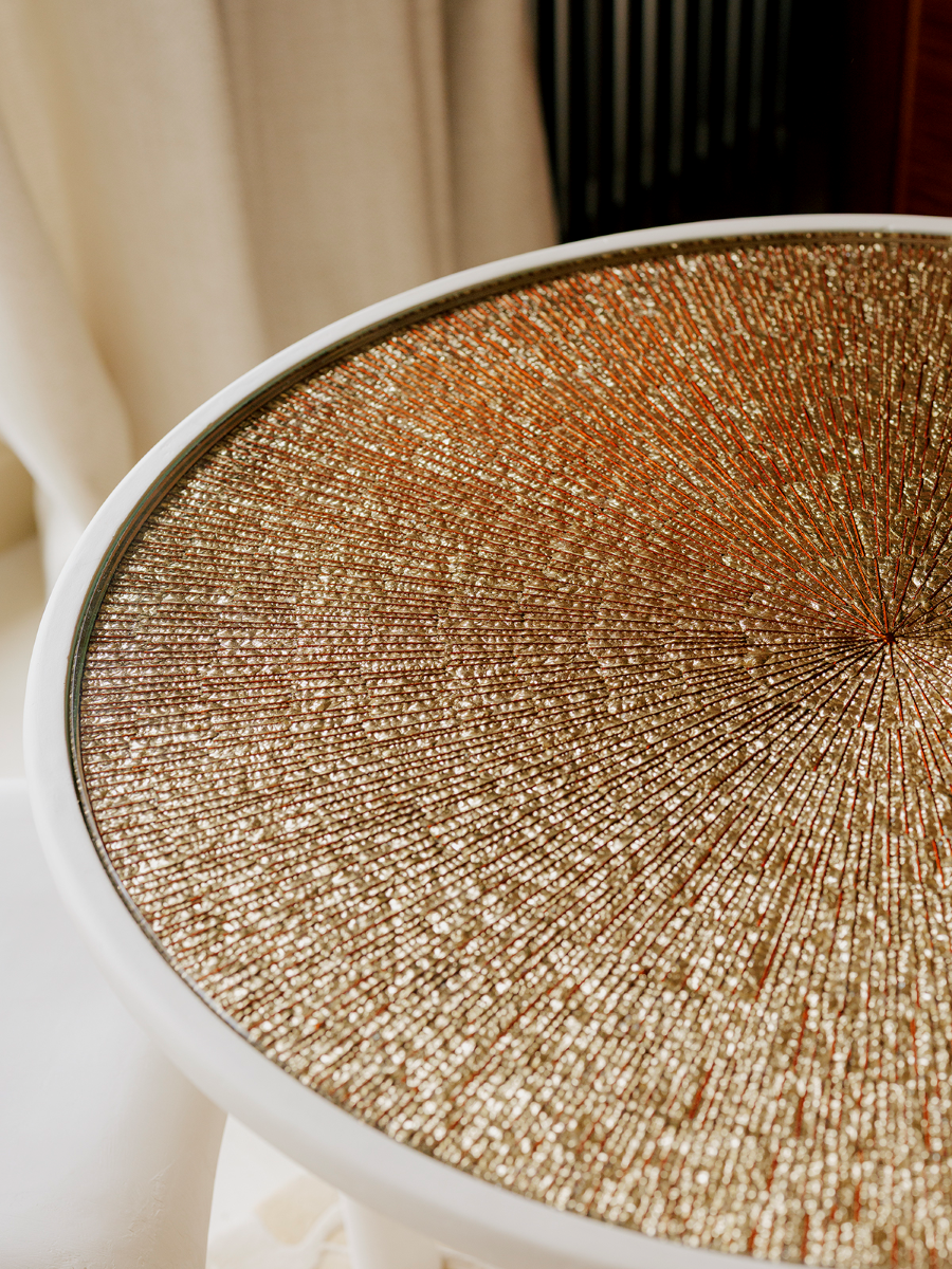 Élégance sculpturale et savoir-faire d’exception s’unissent dans la table d’appoint Bellezza, pièce unique née d’une collaboration entre Caroline Andréoni, Staff Espaces Volumes et Atelier Pictet. Présentée à l’occasion de la Biennale Révélations 2025, elle incarne l’art décoratif contemporain dans toute sa richesse.

Le plateau en verre est magnifié par une gravure en ronde-bosse, buriné avec précision, puis doré à la feuille d’or Moongold, une teinte précieuse aux reflets chauds et lumineux. 