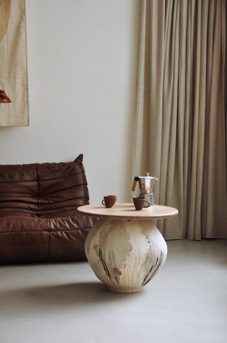 Table basse conçue et fabriquée par la céramiste Marguerite Porche. Le large piétement en grès est inspiré des jarres anciennes et parcouru d’éclats de roche glanés à Bormes-les-Mimosas. La surface du pied de cette table est travaillée de telle manière que des couches de grès, d’engobe et d’émail se superposent les unes aux autres créant ainsi un jeu  visuel et de textures sur chaque face.