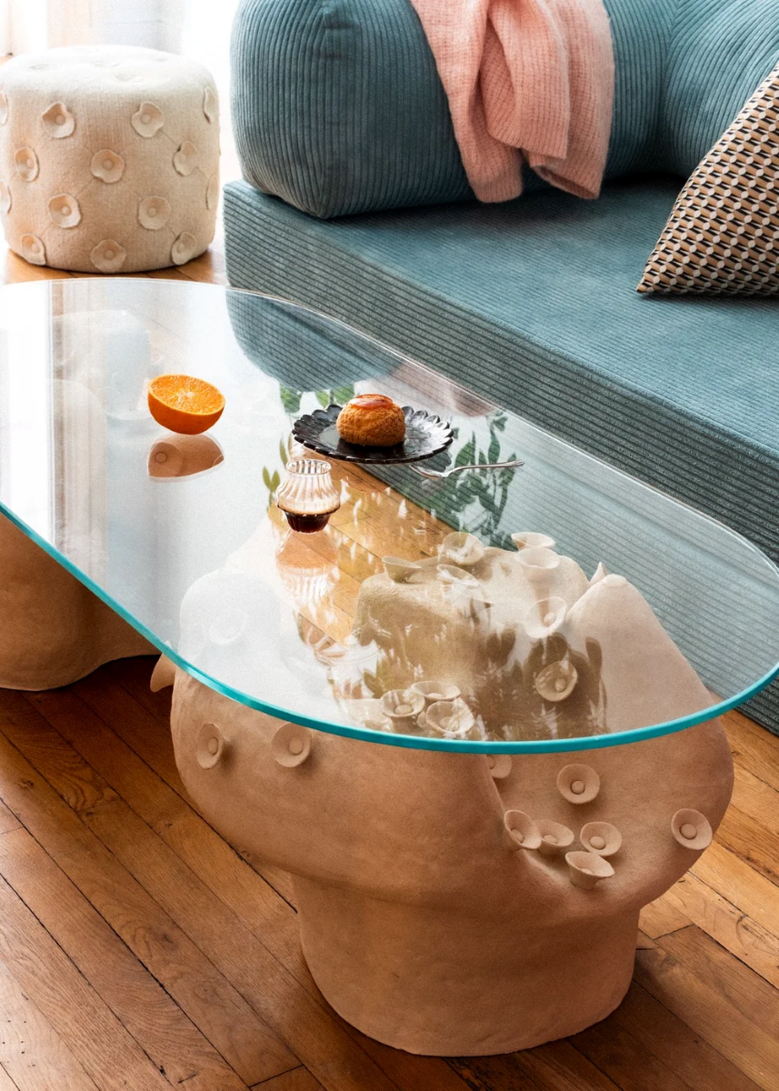 Table basse conçue et fabriquée par la céramiste Marguerite Porche. Deux larges pieds en grès blanc aux courbes sinueuses évoquant la roche sculptée par les éléments et parcourue de petites fleurs cherchant le soleil, portent un large plateau en verre d’un cm d’épaisseur. 