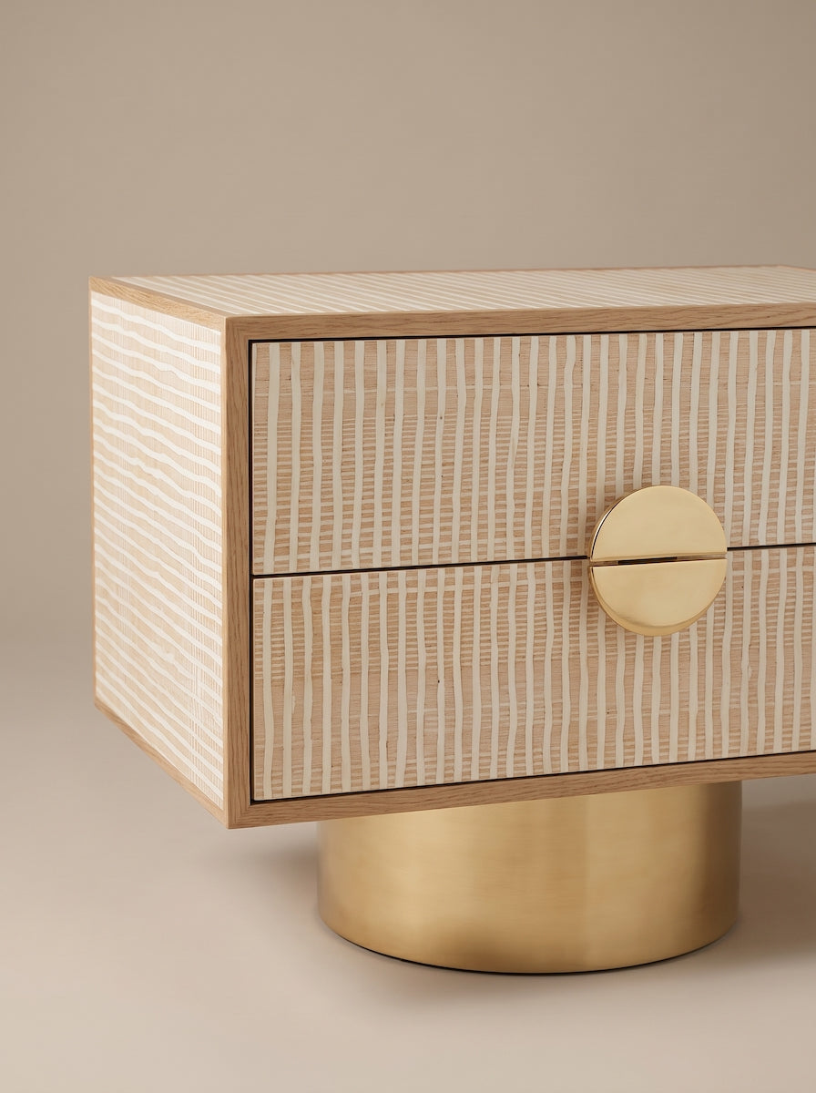Paire de tables de chevet FAENA, imaginée par Caroline Andreoni pour la master bedroom d'une villa privée à Miami. Le caisson en chêne massif s'habille d'un placage en bois graphique aux tons ivoire et sable, posé sur un socle cylindrique en laiton poli.

Les photos affichées correspondent à la version la plus grande des chevets.