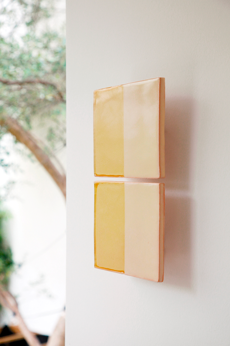 Les Tiles sont des appliques murales conçues par Violaine d'Harcourt en collaboration avec la designer hollandaise Marianne Smink. Utilisant le procédé de la sérigraphie, l'applique Tiles G est ainsi colorée d'un jaune et d'un beige représentant la céramique brute. L'ampoule, cachée derrière un carreau, diffuse un éclairage indirect, créant un effet de clair-obscur et un éclairage très doux.